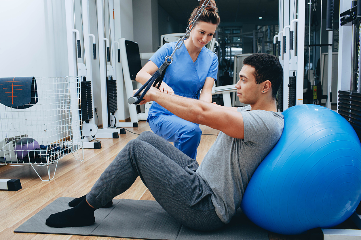 kinesiologist helps a mixed race man doing exercises to strengthen his back muscles. treatment of back pain using kinesitherapy.